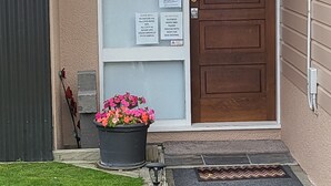 A house entrance with a wooden door, a glass panel, and a sign with rules. There is a flower pot with flowers in front. - Barnes Street BNB - Enjoy your stay in lovely private unit.
 (Timaru)