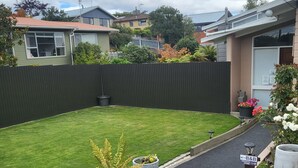 A well-maintained residential backyard with a neatly trimmed lawn, potted plants, and a pathway leading to a private home. - Barnes Street BNB - Enjoy your stay in lovely private unit.
 (Timaru)