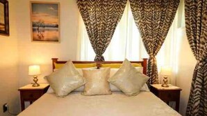 A hotel room with a bed, two bedside tables with lamps, and patterned curtains. - Barnes Street BNB - Enjoy your stay in lovely private unit.
 (Timaru)