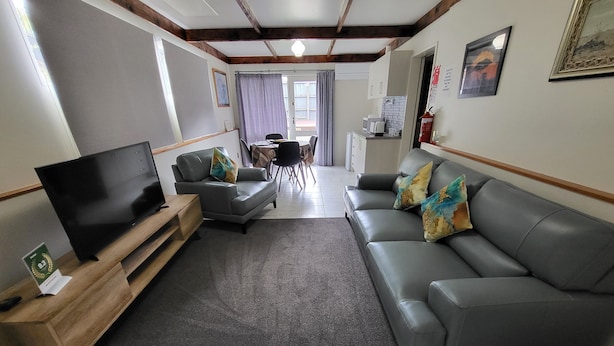 A modern living room with a grey sofa, a television, and a coffee table. There is a dining area in the background with a table and chairs. - Barnes Street BNB - Enjoy your stay in lovely private unit.
 (Timaru)