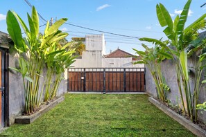 A courtyard with a concrete wall, a metal gate, and large green plants. - Jaci Residence Umalas By Betterplace (Kerobokan)