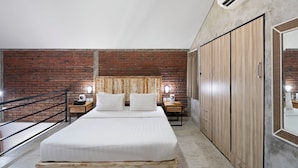 Een slaapkamer met een bakstenen muur, een groot bed, een houten garderobe en een klein nachtkastje met een lamp.