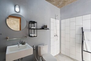 A modern bathroom with a white sink, round mirror, and a glass shelf with toiletries. - Jaci Residence Umalas By Betterplace (Kerobokan)