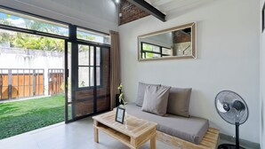 Een moderne woonkamer met een bank, een salontafel, een ventilator en een groot raam met uitzicht op een tuin.