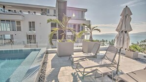 Un área de piscina moderna al aire libre con sillones de descanso y vistas al mar.