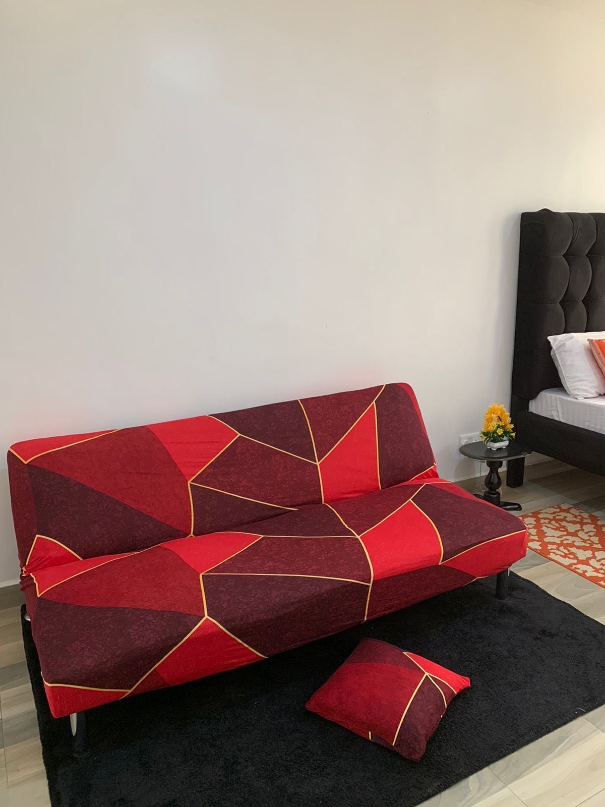 A modern living room with a red and black sofa, a black rug, and a small side table with a vase of flowers.