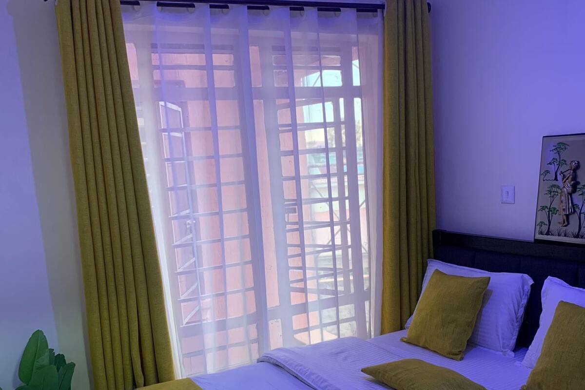 Una habitación de hotel con cama, cortinas, ventana con vistas y una obra de arte en la pared.
