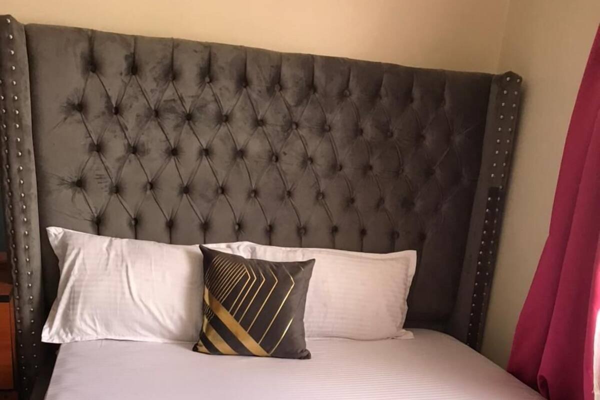 Una cama con cabecera capitonada, dos almohadas y una colcha impecable.