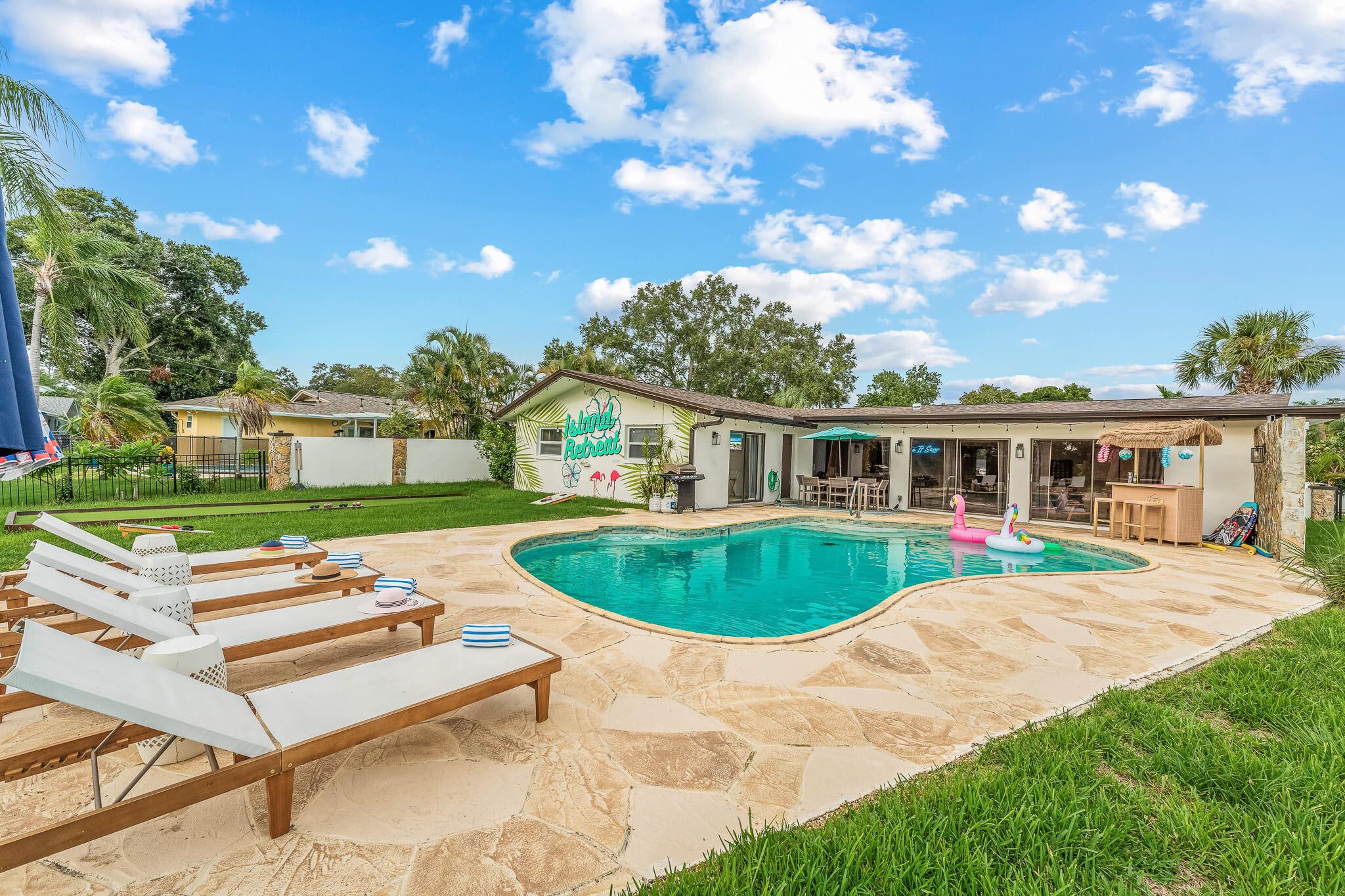 A backyard with a swimming pool, lounge chairs, and a house with a 'Beach House' sign.