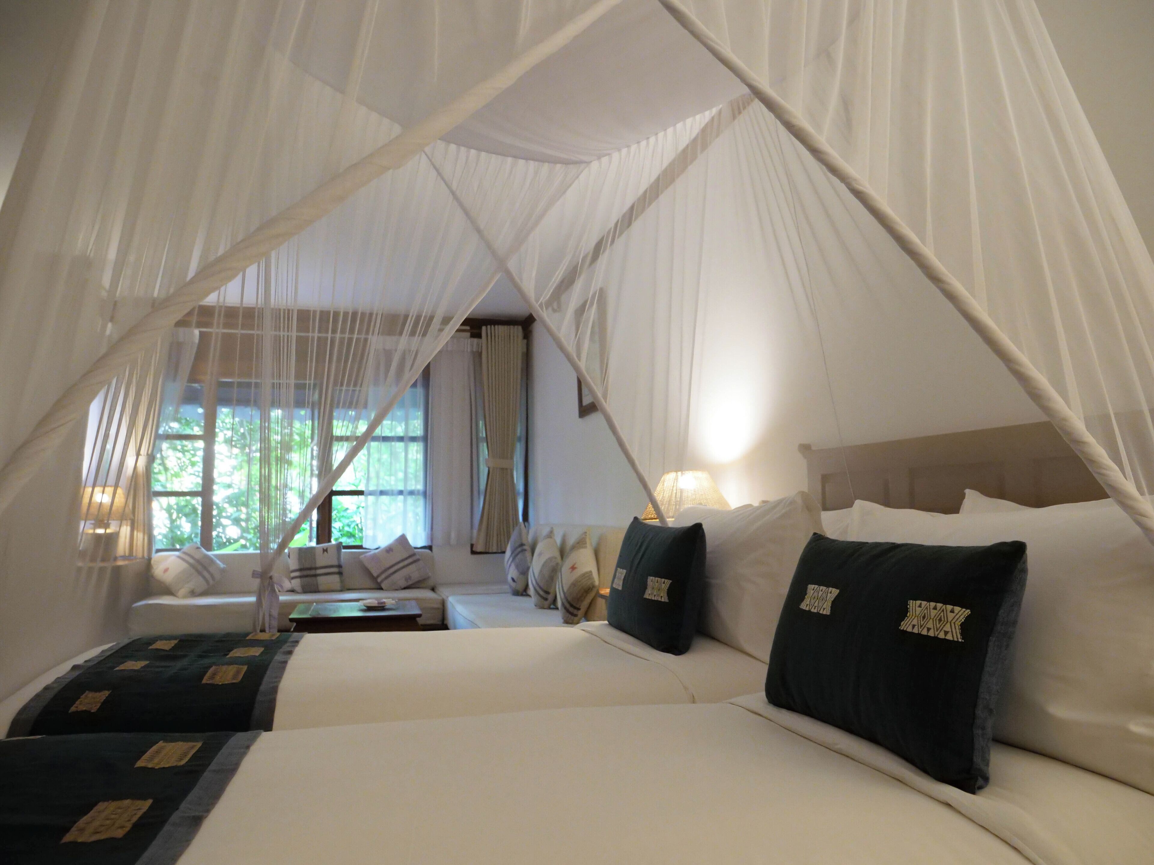 A room with a canopy bed, a sofa, and a window with curtains.