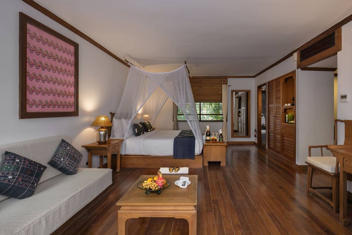 A hotel room with a bed, a sofa, a wooden coffee table, a desk, and a TV.