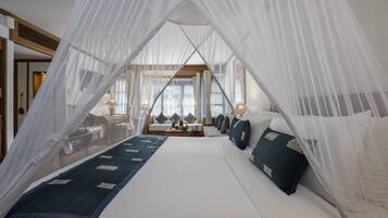 Quarto com cama de dossel, um espaço de estar com sofá e uma mesa, e vista para o exterior por grandes janelas.
