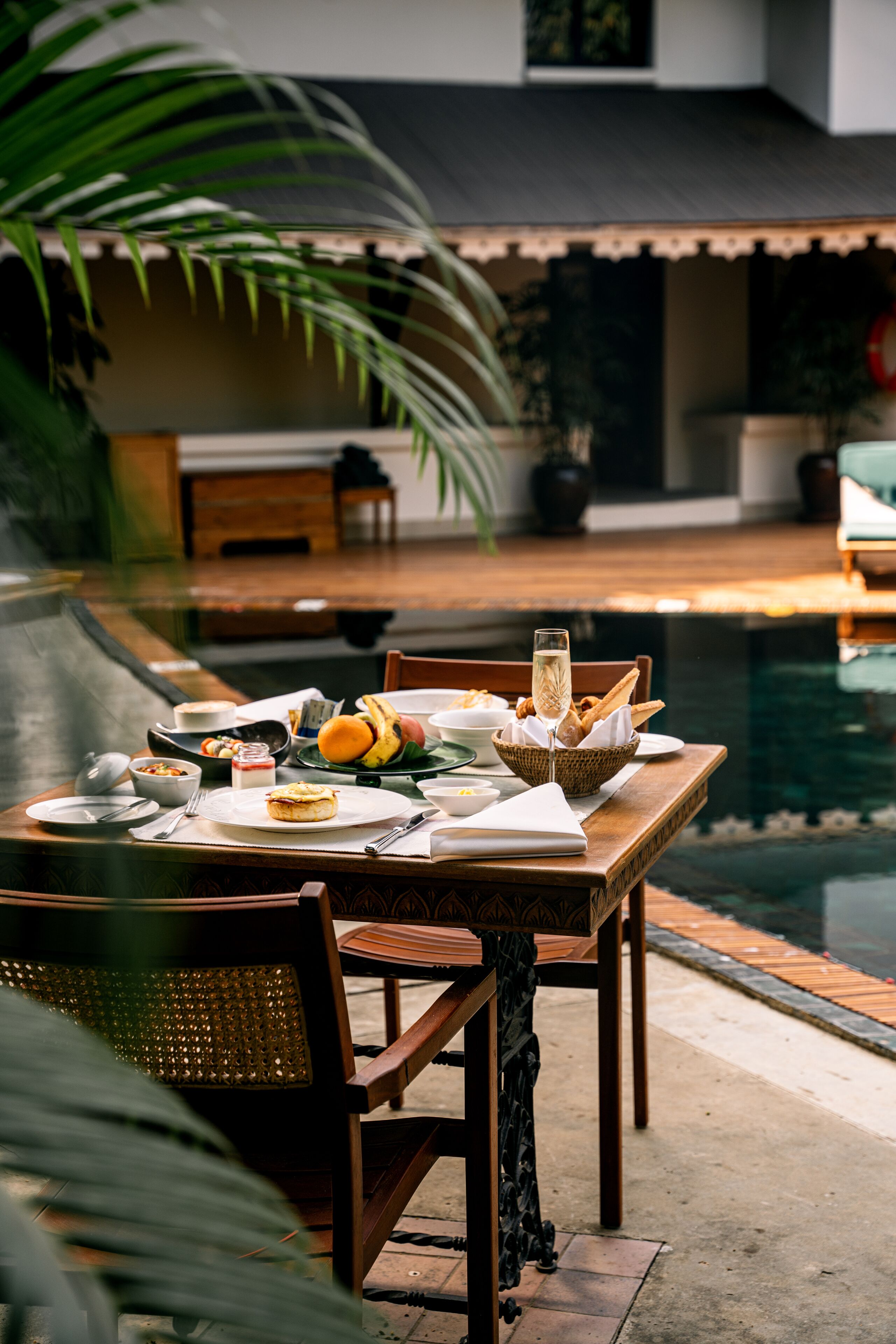 A dining table set with plates, glasses, and food, overlooking a pool.