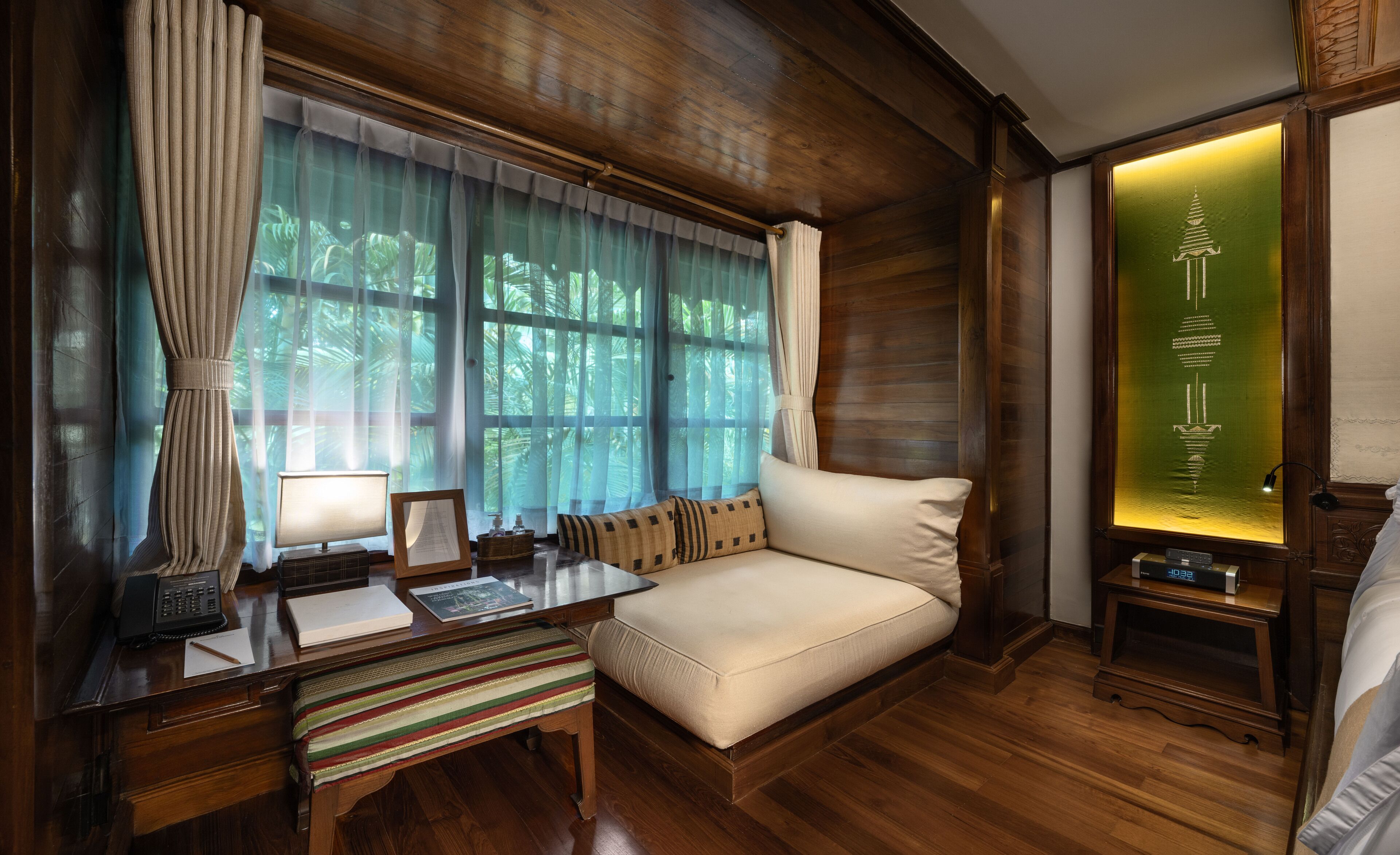 A cozy room with a wooden desk, a cushioned bench, and a sofa.
