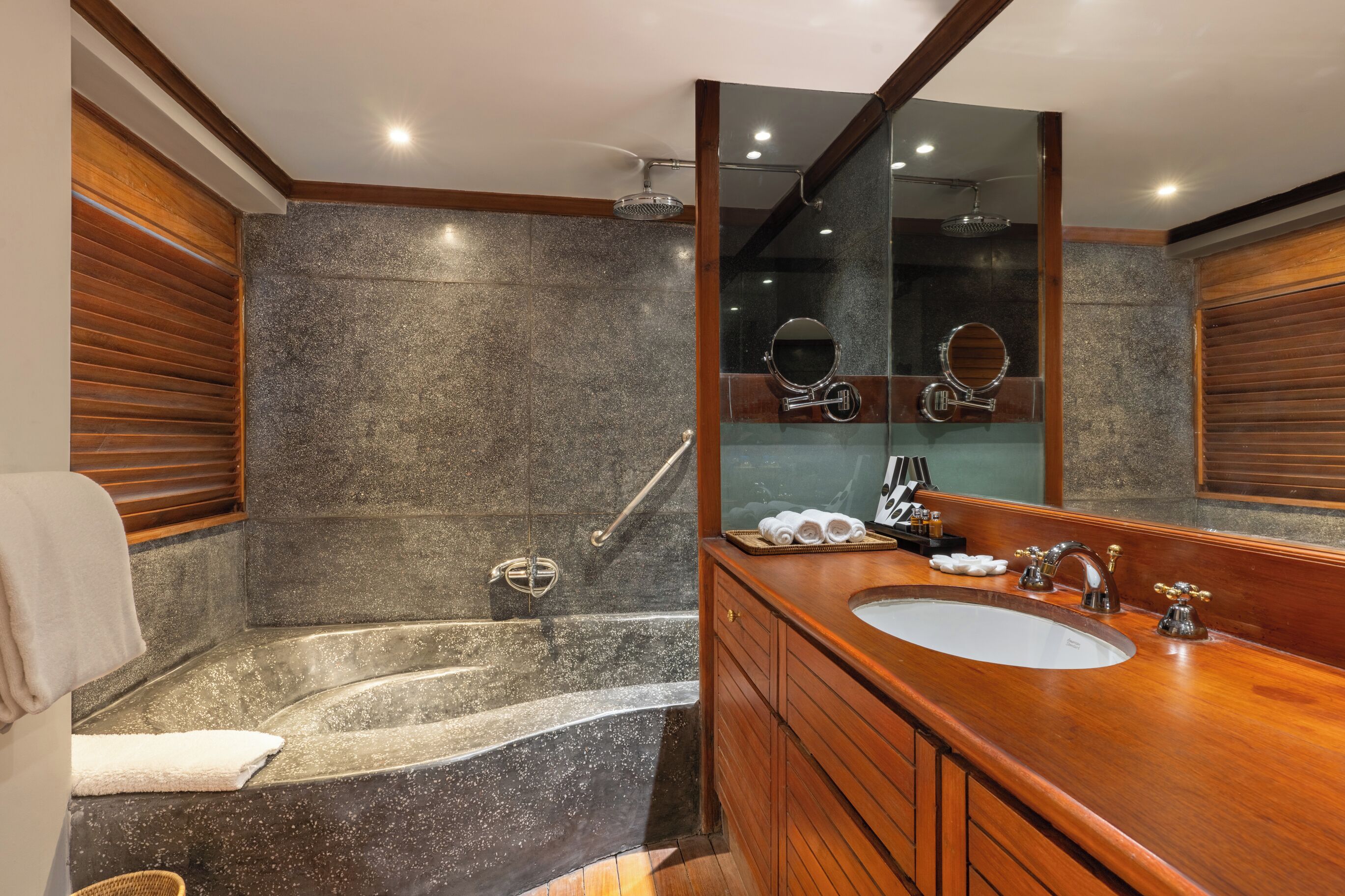 Une salle de bain avec une douche en granit, un meuble-lavabo en bois et un grand miroir.