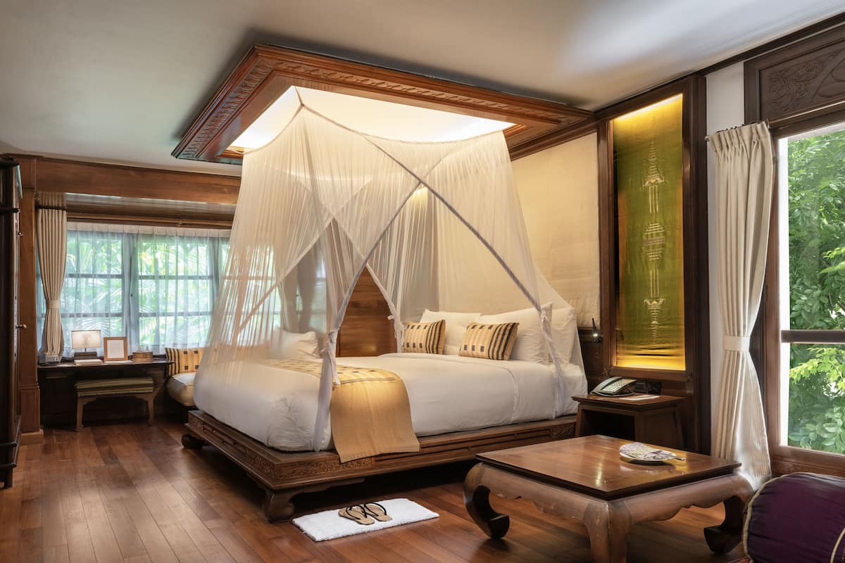 A traditional-style bedroom with a canopy bed, wooden furniture, and a view of greenery outside.