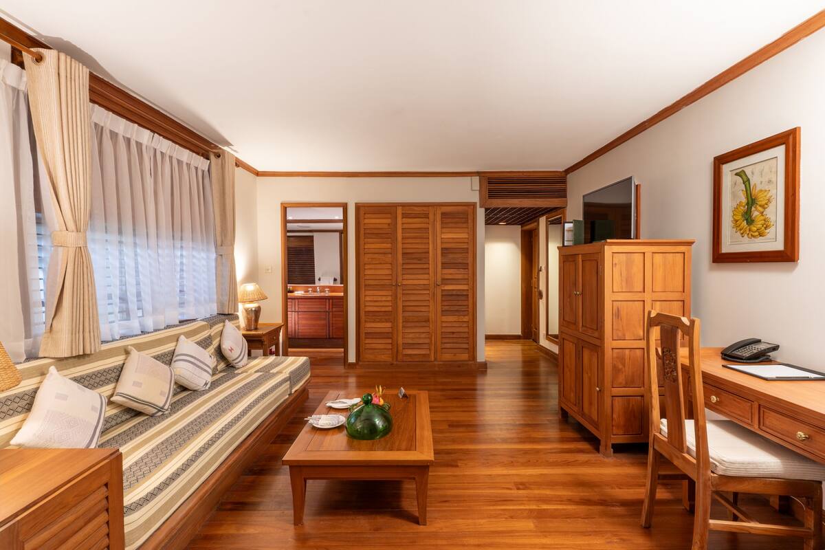 A room with a wooden sofa, a dining table, a wooden desk, and a cabinet.