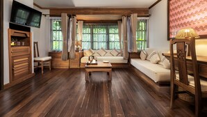 Een gezellige woonkamer met houten vloer, een bank, een salontafel, een aan de muur bevestigde televisie en een raam met gordijnen.