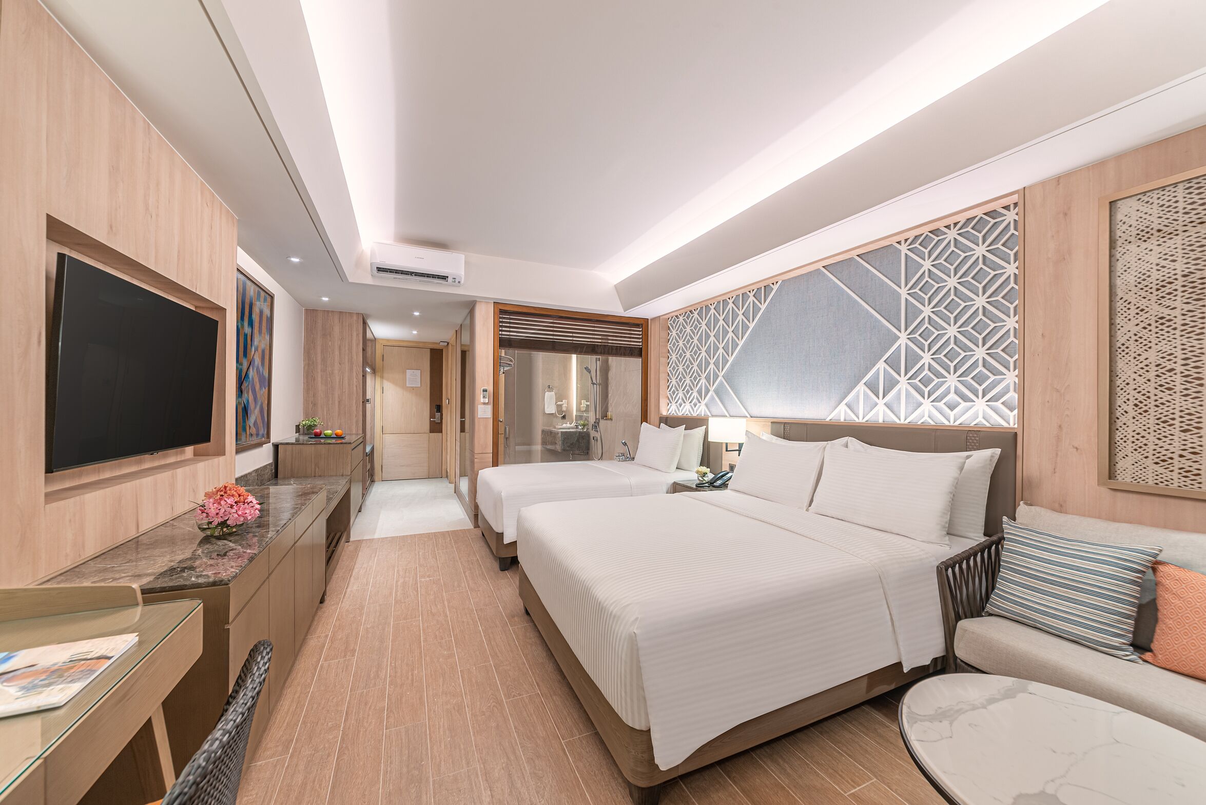 A modern hotel room with a large bed, a desk, a TV, and a bathroom visible through an open door.