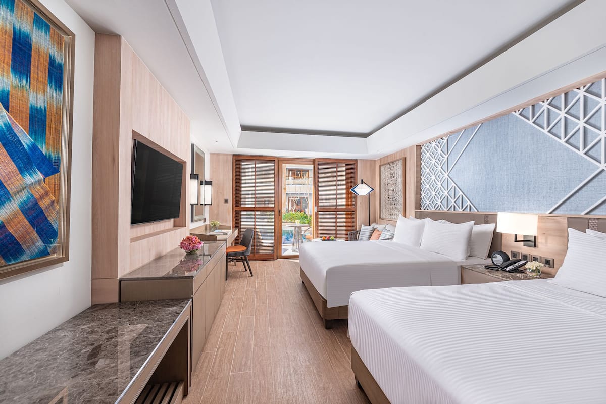 A modern hotel room with a large bed, a desk with a chair, a television, and a view of the outdoors through a sliding door.
