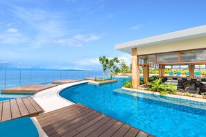 A modern infinity pool with a wooden deck, surrounded by lush greenery and a view of the ocean. - Henann Premier Coast Resort (Panglao)