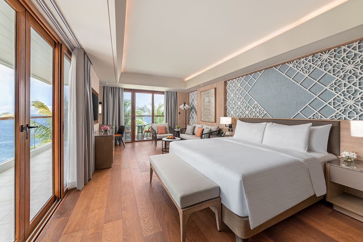 A spacious bedroom with a large bed, a seating area with a table, and a balcony with a view of the ocean.
