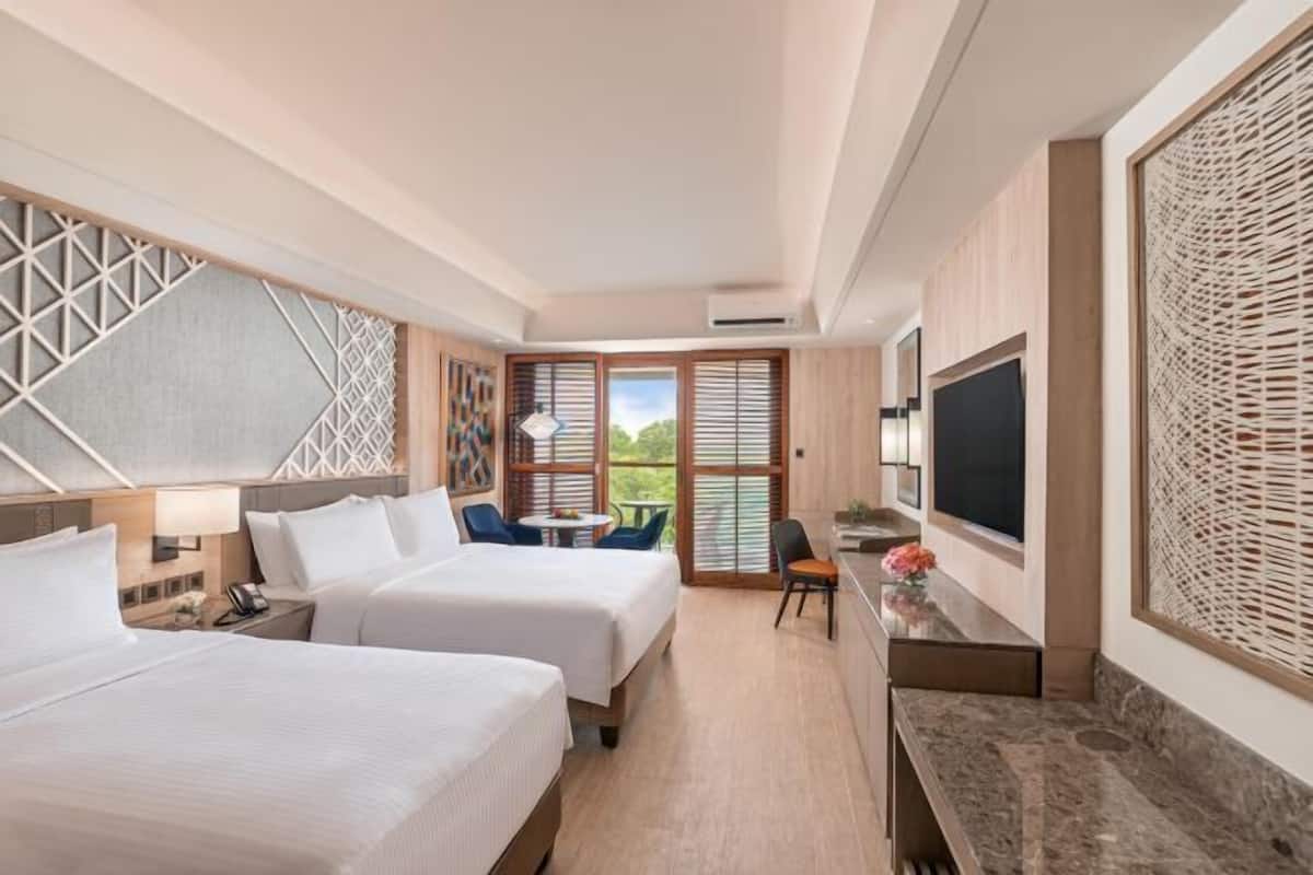 A hotel room with two beds, a desk, a TV, and a balcony with a view.