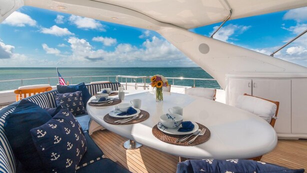 A dining area on a boat with a view of the sea, a table set for two, and a flag. - Stonehedge at Sea (Fort Lauderdale)