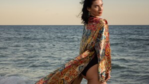 A person standing on a beach with a colorful shawl, facing the ocean. - Stonehedge at Sea (Fort Lauderdale)