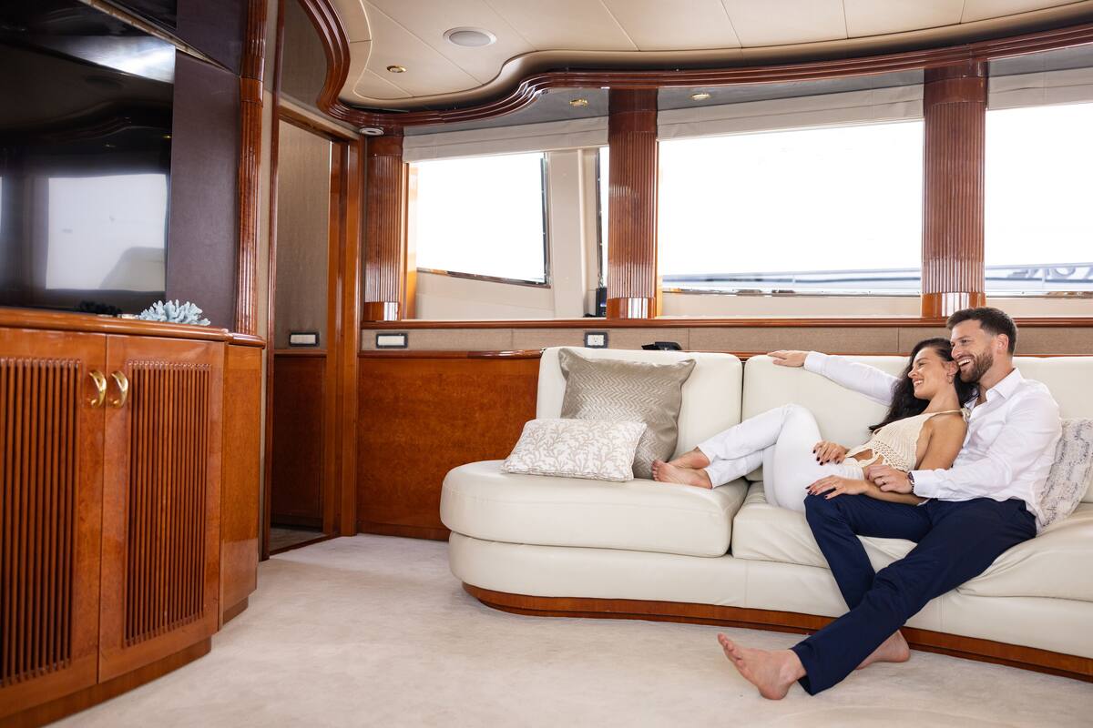 A couple on a curved white sofa with a wooden cabinet and large windows in a cabin-style room.