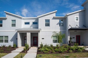 A modern two-story residential building with a stone facade, a red front door, and a small porch area. - Family Fun in Near Disney Star Wars, Pool, BBQ (Kissimmee)