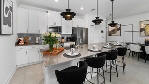 A modern kitchen with white cabinets, a central island with bar stools, and pendant lighting. - Family Fun in Near Disney Star Wars, Pool, BBQ (Kissimmee)