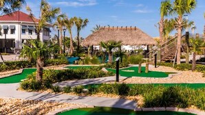 A golf course with a thatched-roof building, palm trees, and a pool area. - Family Fun in Near Disney Star Wars, Pool, BBQ (Kissimmee)