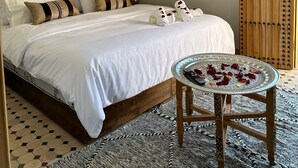 A bedroom with a large bed, a wall-mounted air conditioner, a wooden door with metal studs, and a small table with a glass top. - Riad Fes Colors & Spa (Fes)