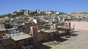 A rooftop terrace with a table and chairs, overlooking a cityscape with buildings and a hill in the distance. - Riad Fes Colors & Spa (Fes)