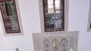 A traditional Moroccan interior with a patterned tile floor, a central chandelier, and a seating area with cushions and a small table. - Riad Fes Colors & Spa (Fes)