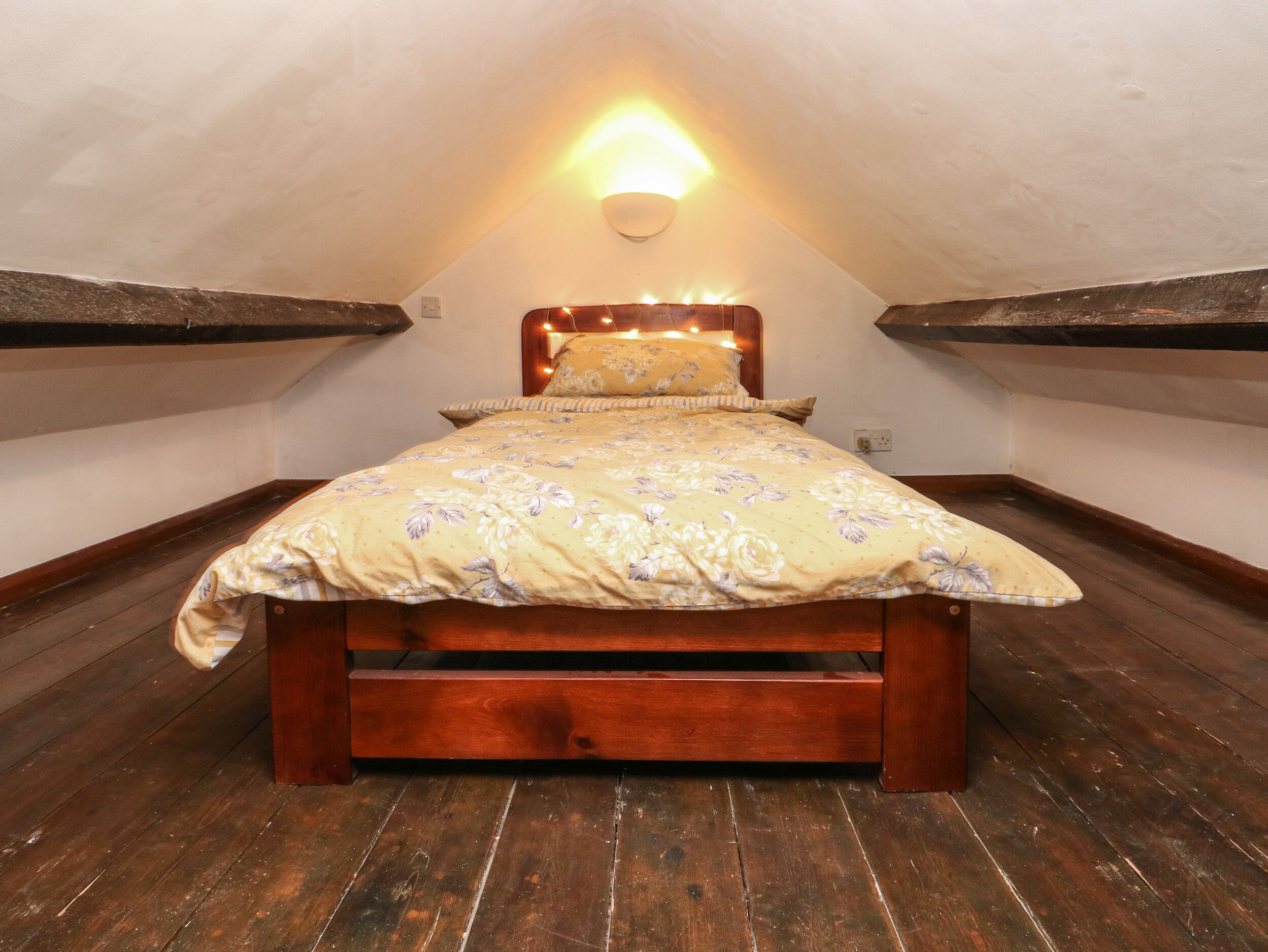 A bedroom with a wooden bed, a sloped ceiling, and a wall-mounted light fixture.