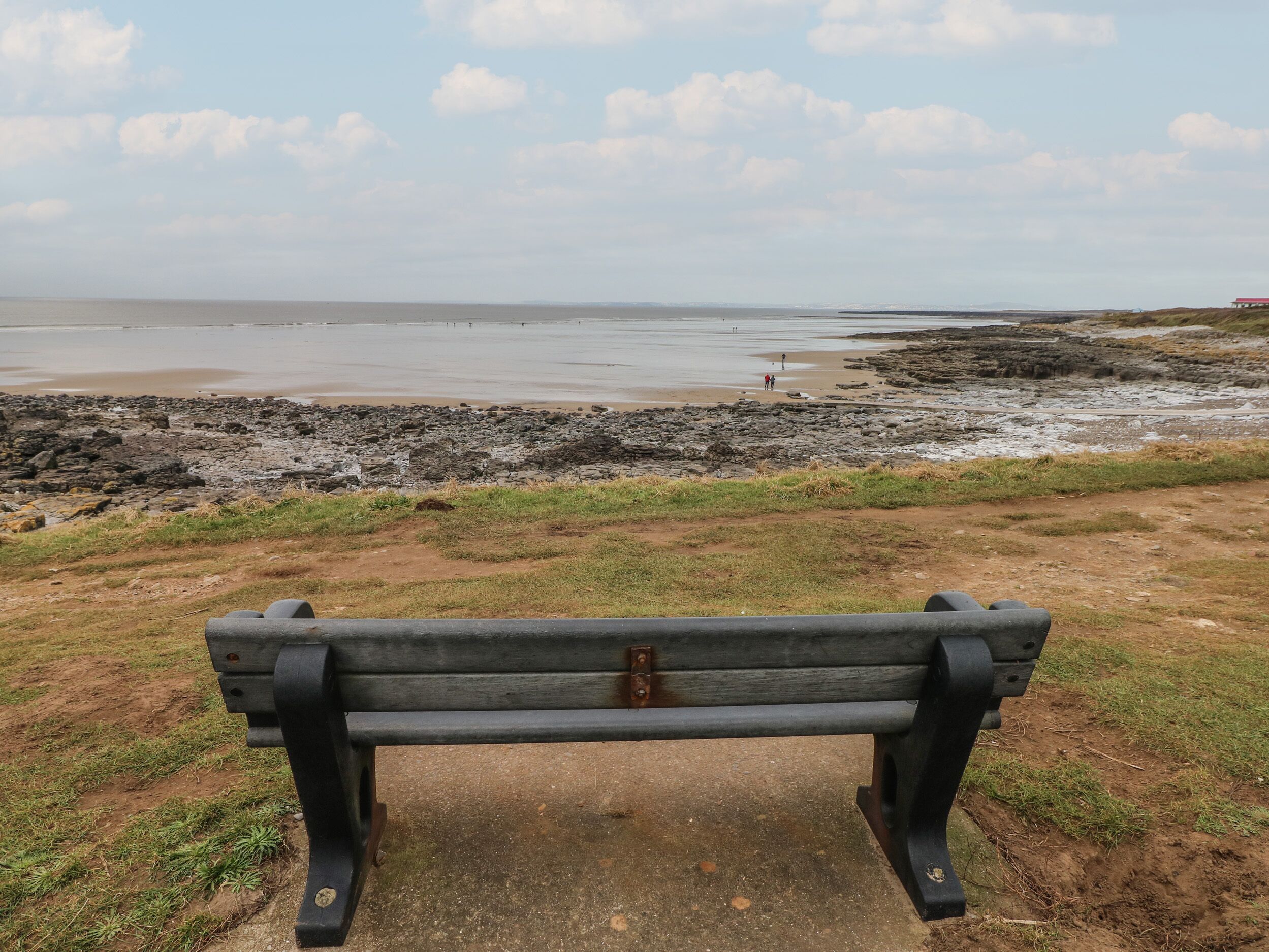 Un banc placé face à une plage rocheuse, offrant une vue sur la mer.