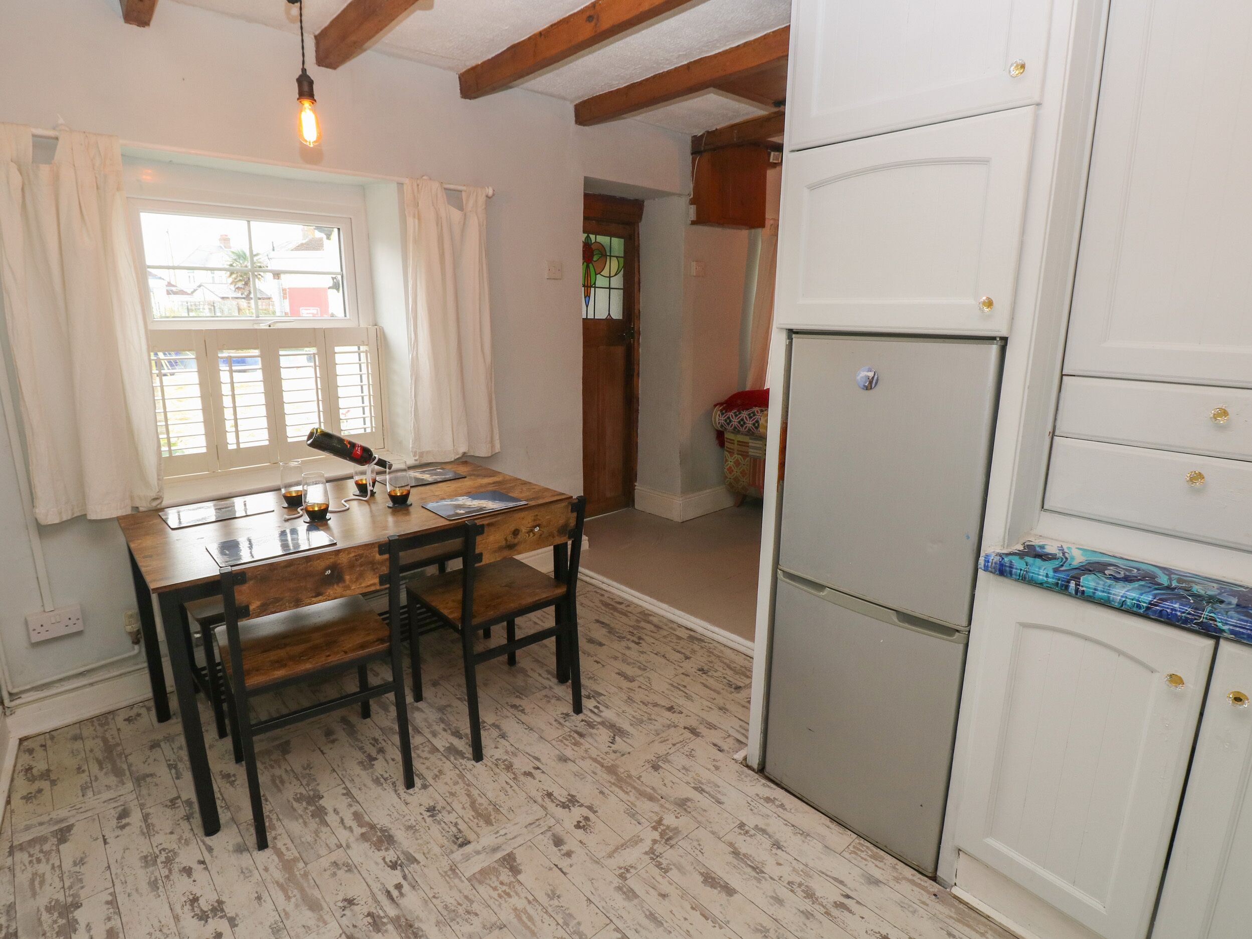 Une cuisine avec une table et des chaises en bois, un réfrigérateur blanc et une fenêtre avec des rideaux.