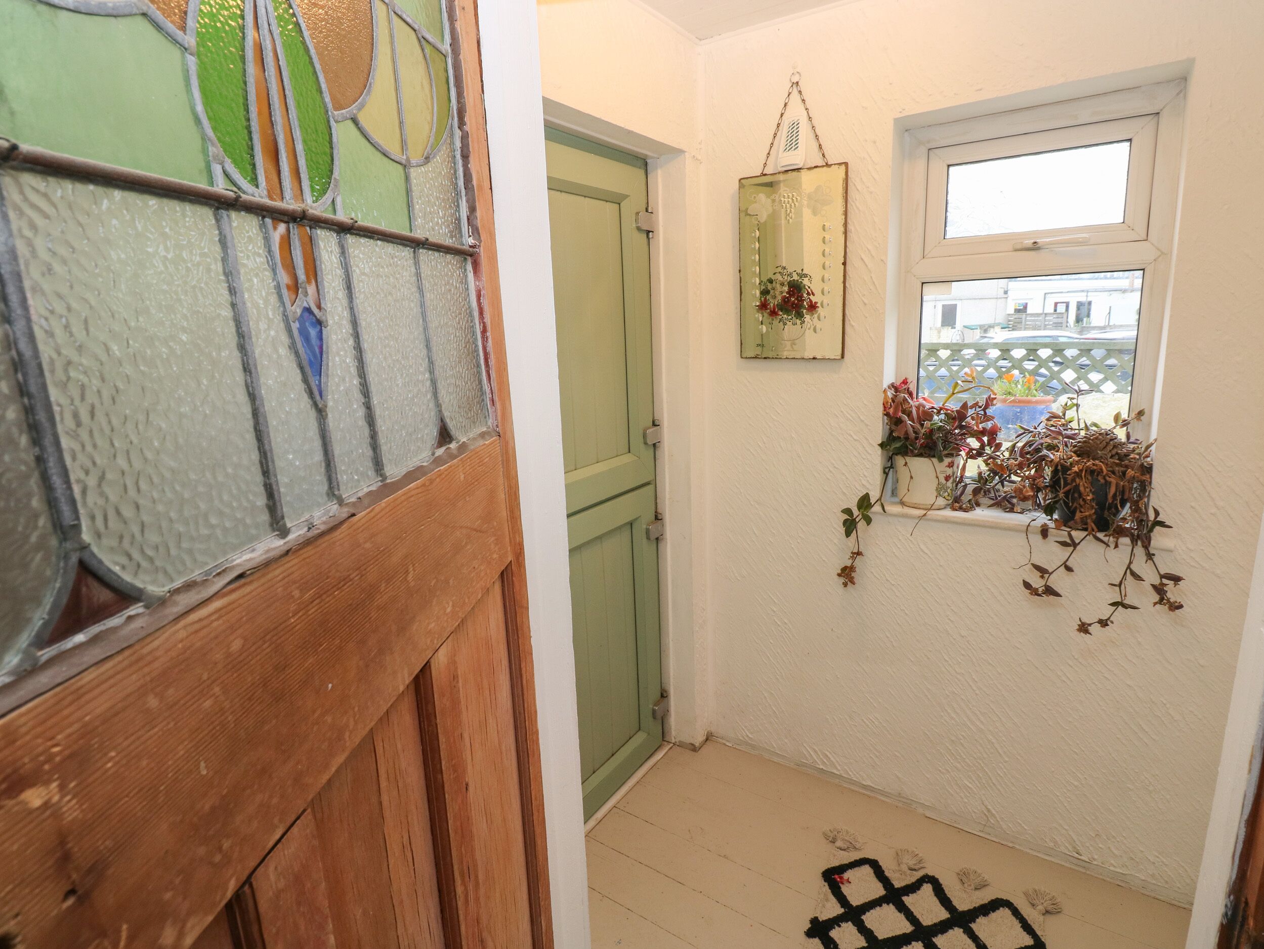 Un pasillo con puerta de madera, una ventana con plantas y un adorno colgante.