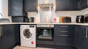 A modern kitchen with dark cabinets, a built-in washing machine, an oven, and a coffee maker.
