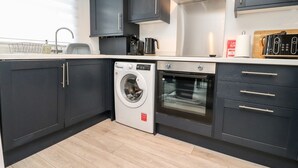 A modern kitchen with dark cabinets, a built-in washing machine, an oven, and a coffee maker.