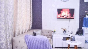 A living room with a tufted sofa, a flat-screen TV, a small white table, and a decorative vase.