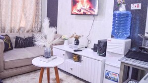 A modern living room with a sofa, a small white table, a TV displaying a fireplace, a water dispenser, and a decorative vase.