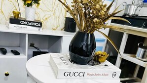 A white table with a black vase and a Gucci watch series album.