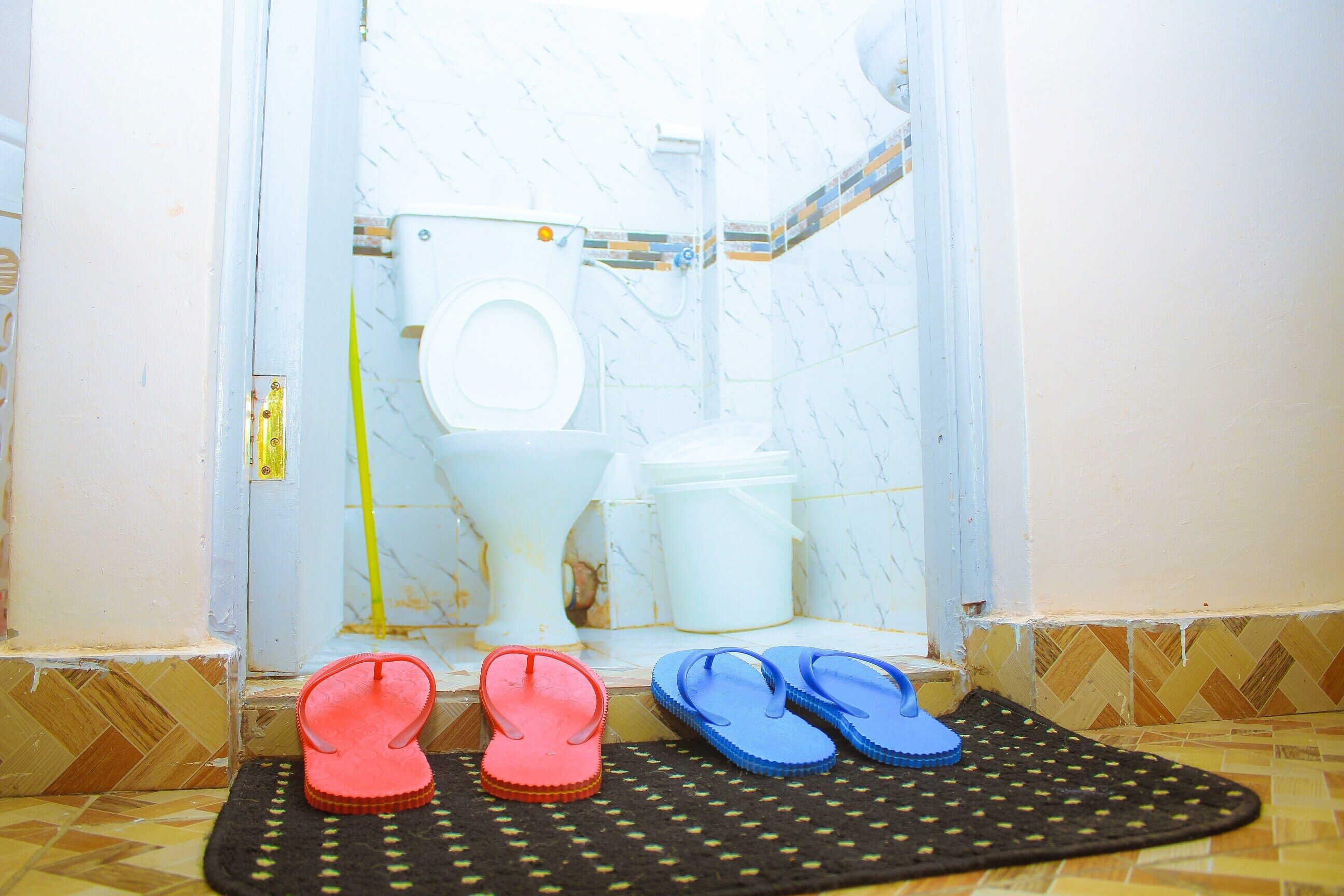 Un baño con inodoro, bidé y una esterilla con chanclas.
