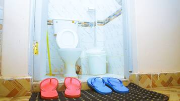 Un baño con inodoro, bidé y una esterilla con chanclas.