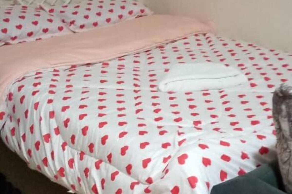 Un lit avec un cadre blanc et une couvre-lit ornée de motifs en forme de cœurs rouges.