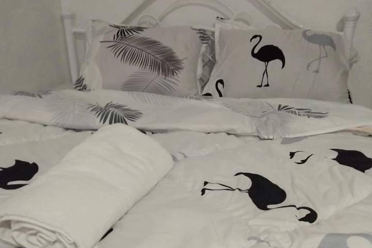 Un lit avec une literie blanche ornée de motifs animaliers noirs, une serviette blanche soigneusement pliée et une tête de lit à motifs floraux.