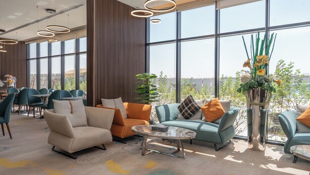 A modern lounge area with seating, a coffee table, and large windows offering a view of the cityscape. - Rosa Grand Hotel Monsieh (Riyadh)